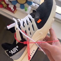 a person holding up a pair of black and white nike air presto